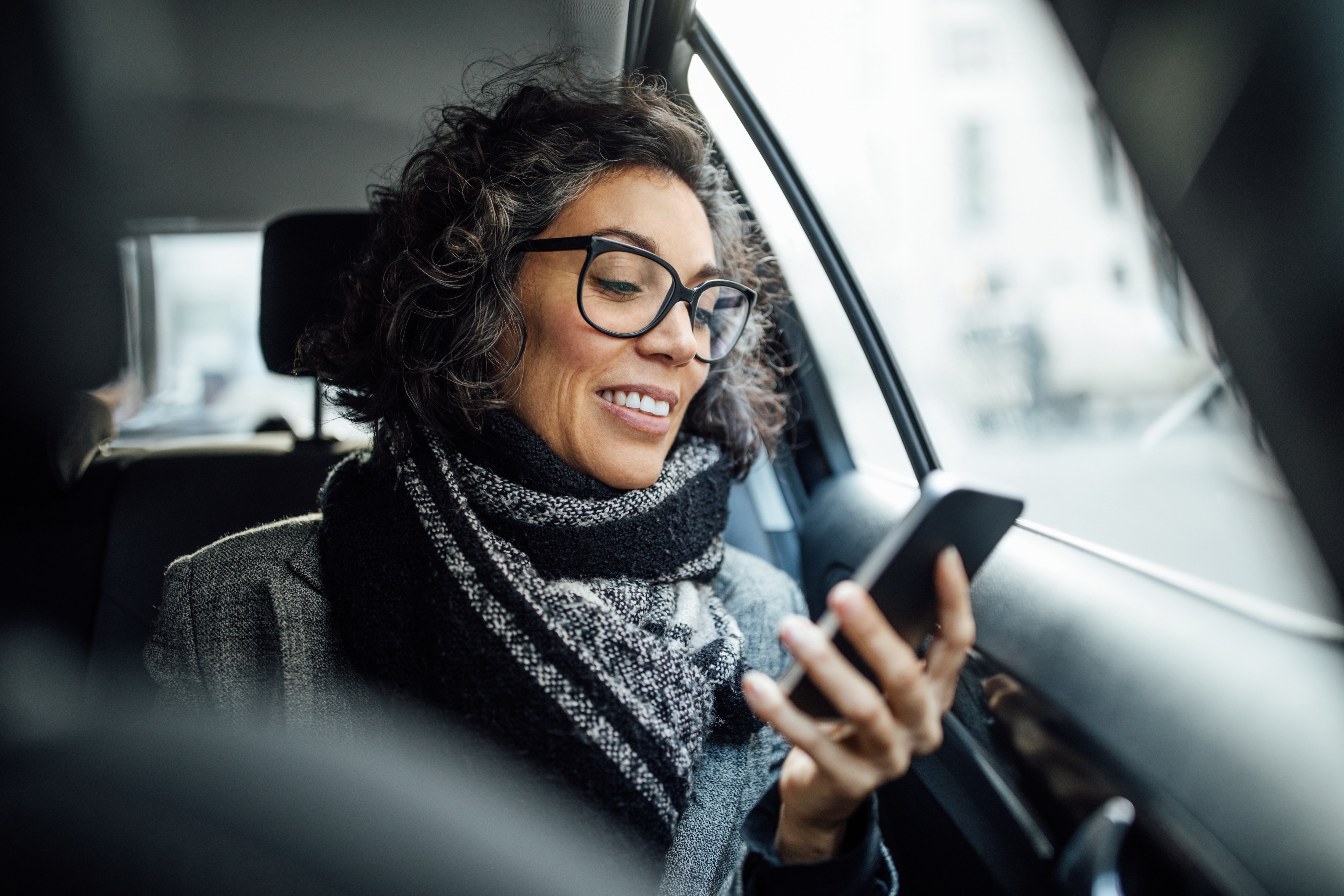 Woman looking at her phone and smiling while taking an Uber to the airport