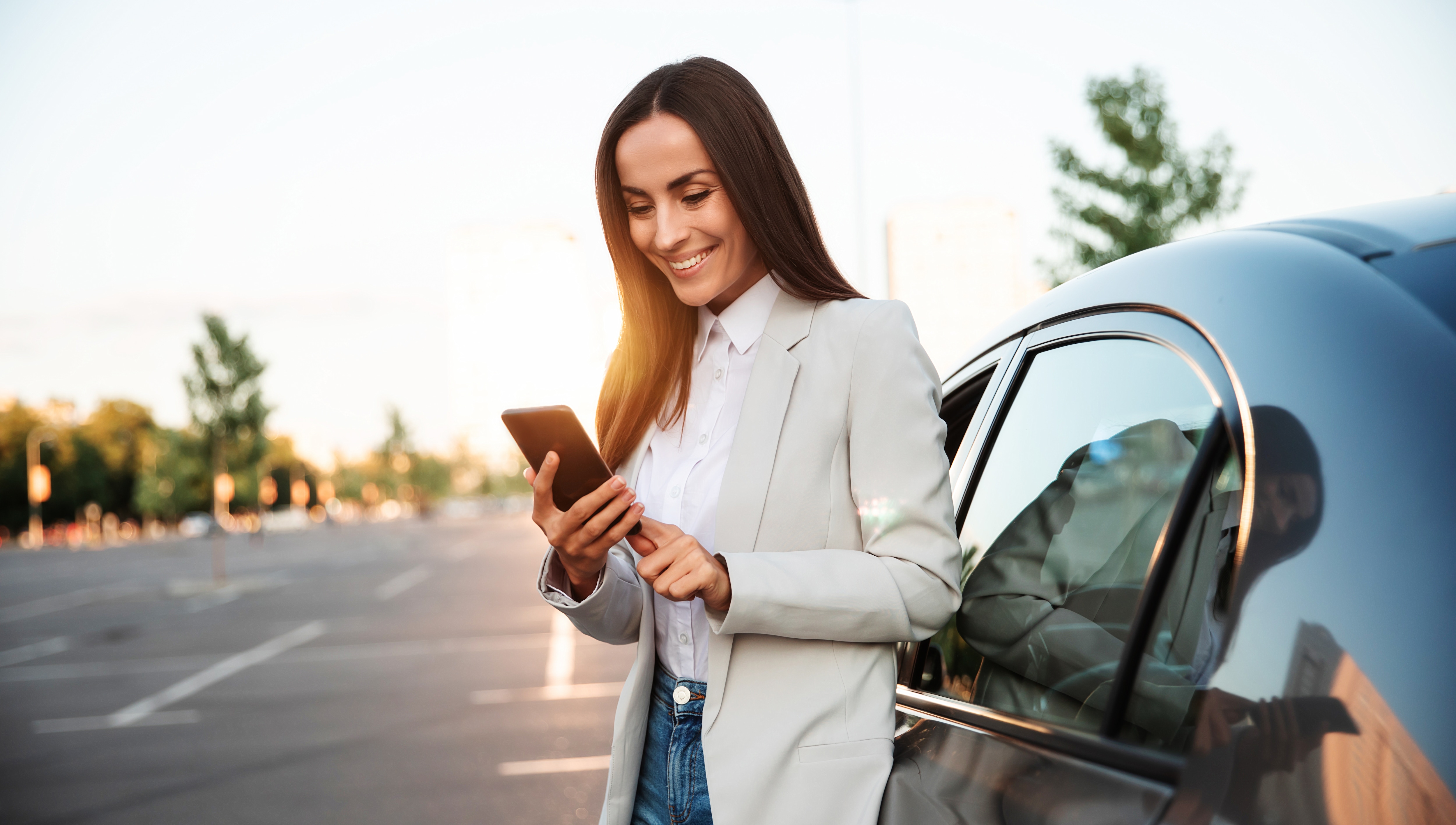 female business traveler standing outside of car looking at phone