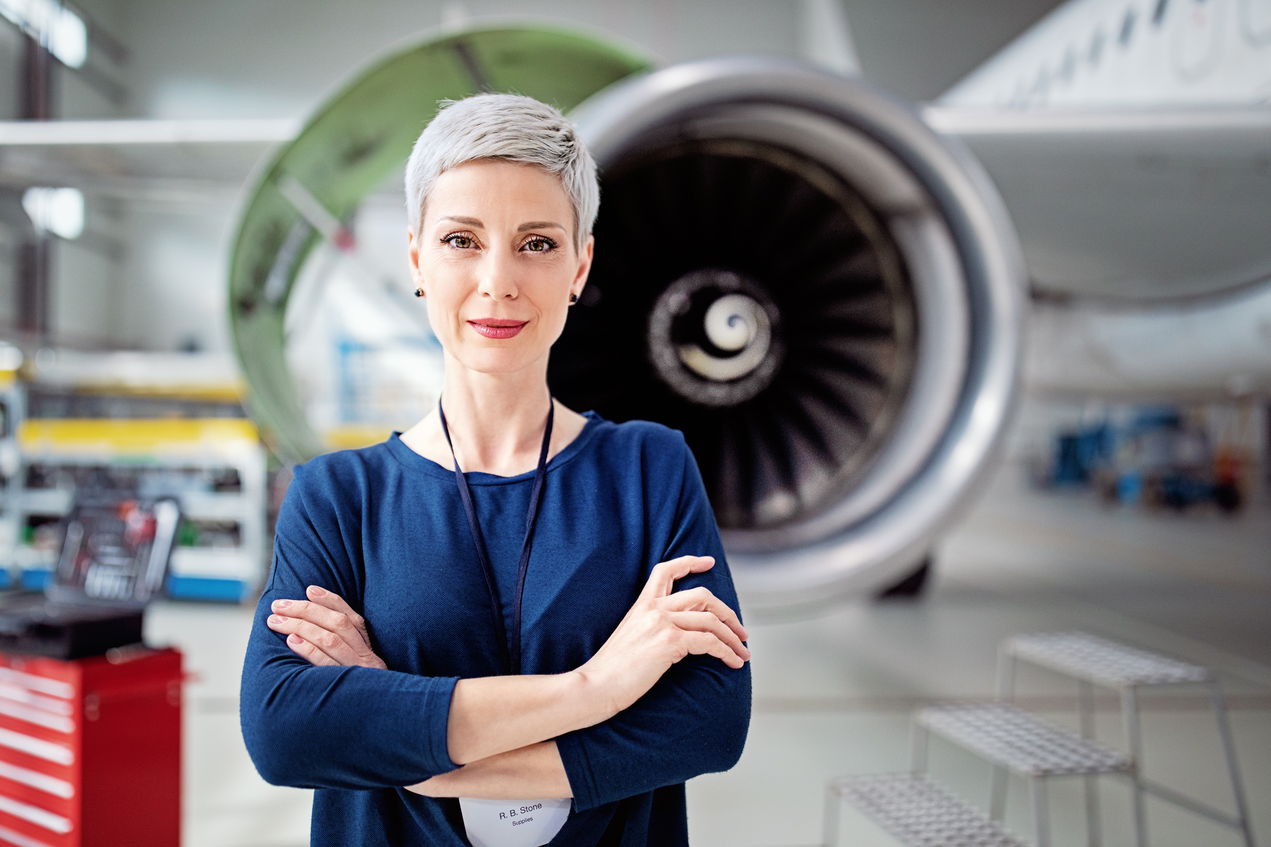 An aerospace worker stands in front of an airplane with arms crossed