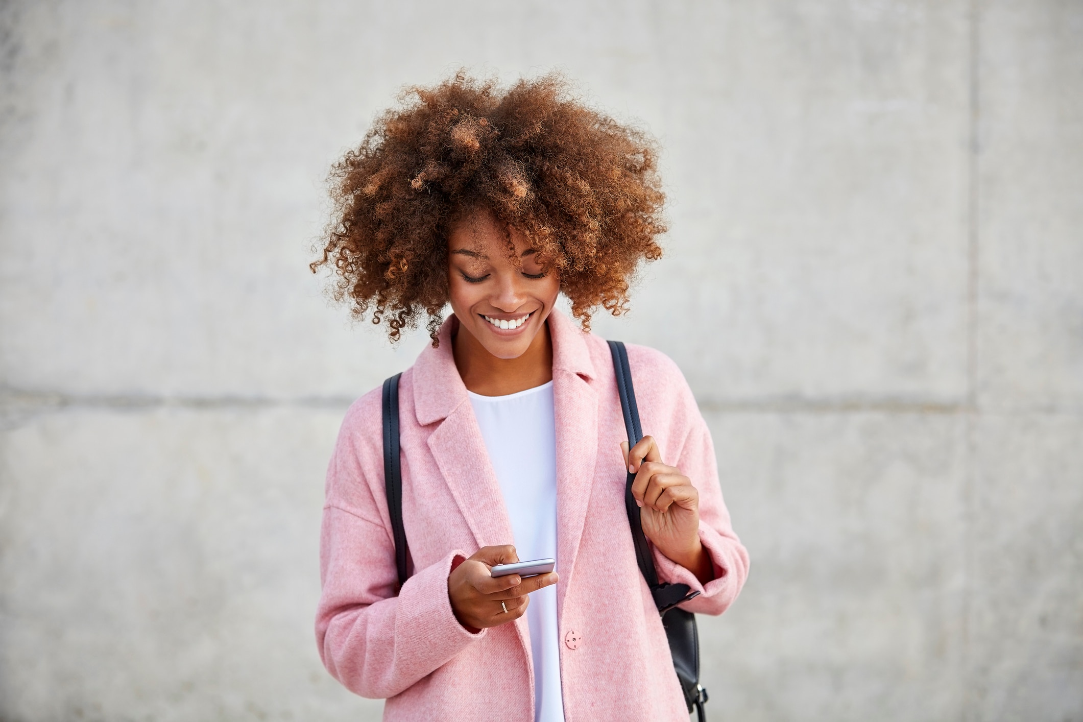 Woman in a pink blazer smiling down at her phone
