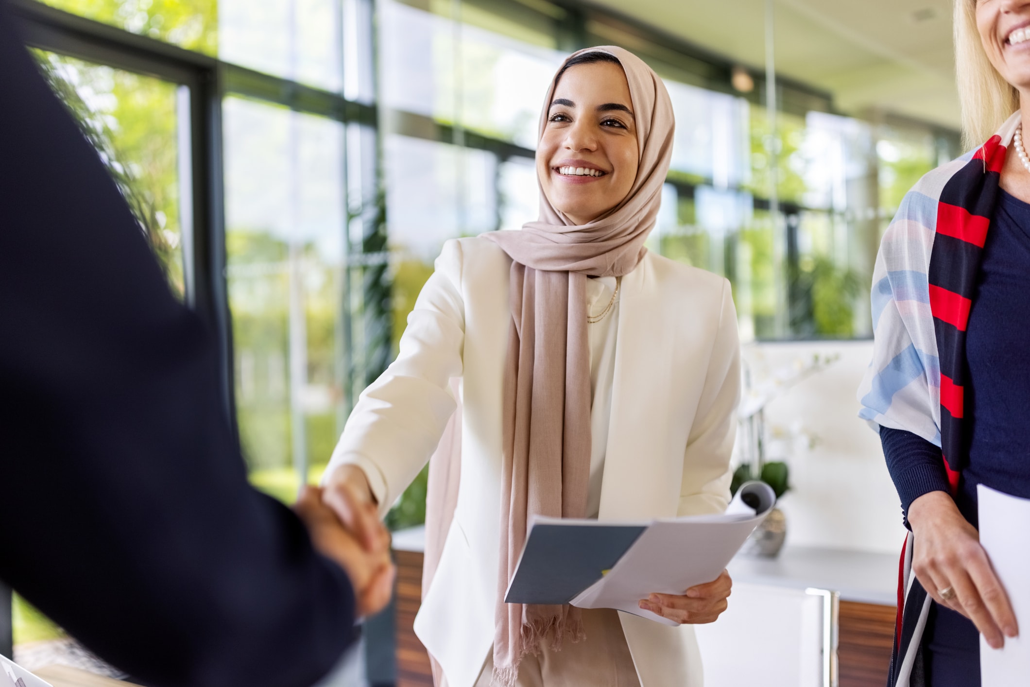 Woman in hijab shaking hands with person mostly off-screen