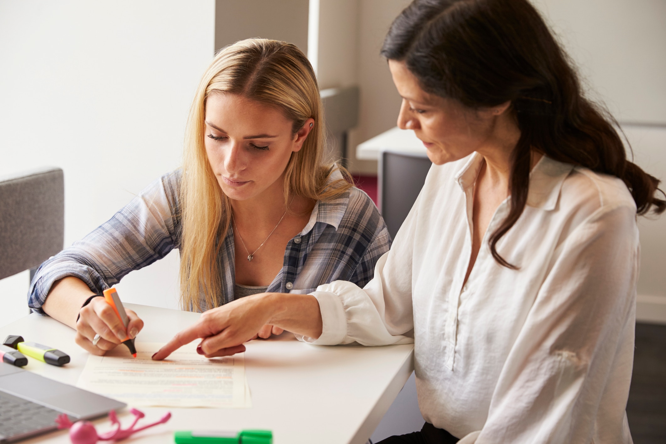 Two seated women looking at a paper on a desk