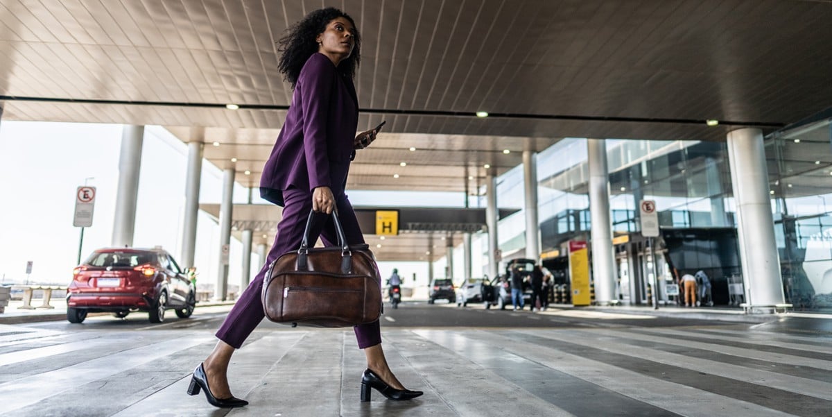 business traveler walking into building, holding cell phone and hand bag