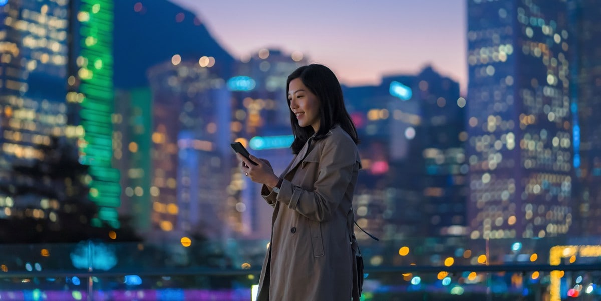 a finance leader smiles while standing in front of a city skyline looking at her mobile phone