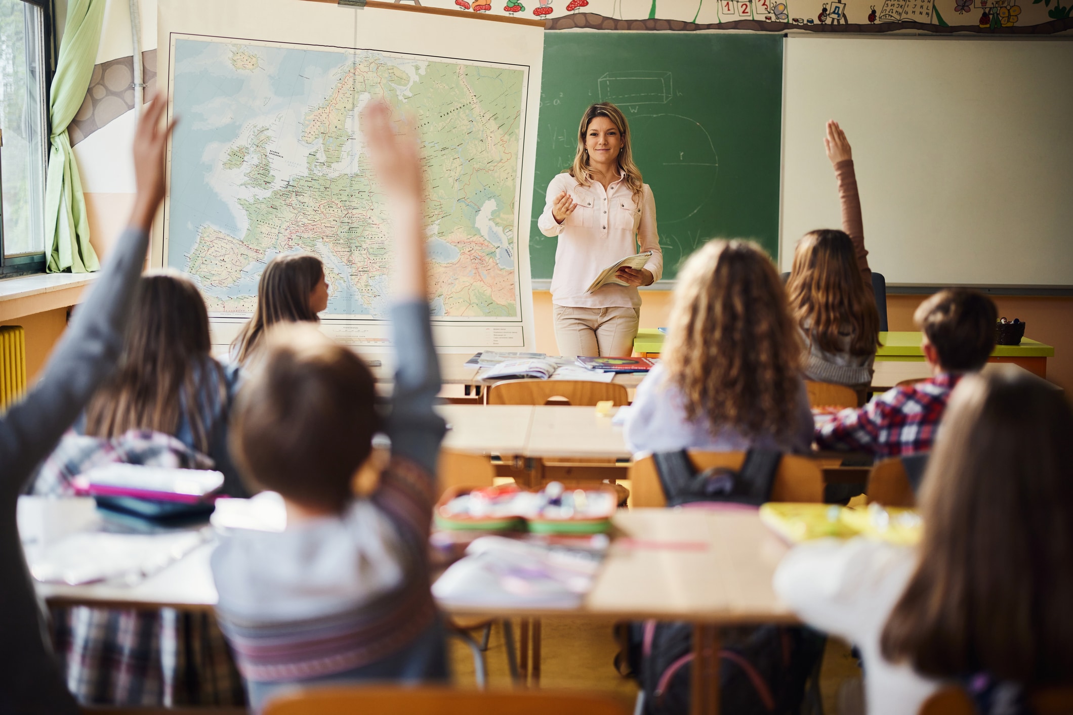 Teacher in a classroom looking at students with their hands raised