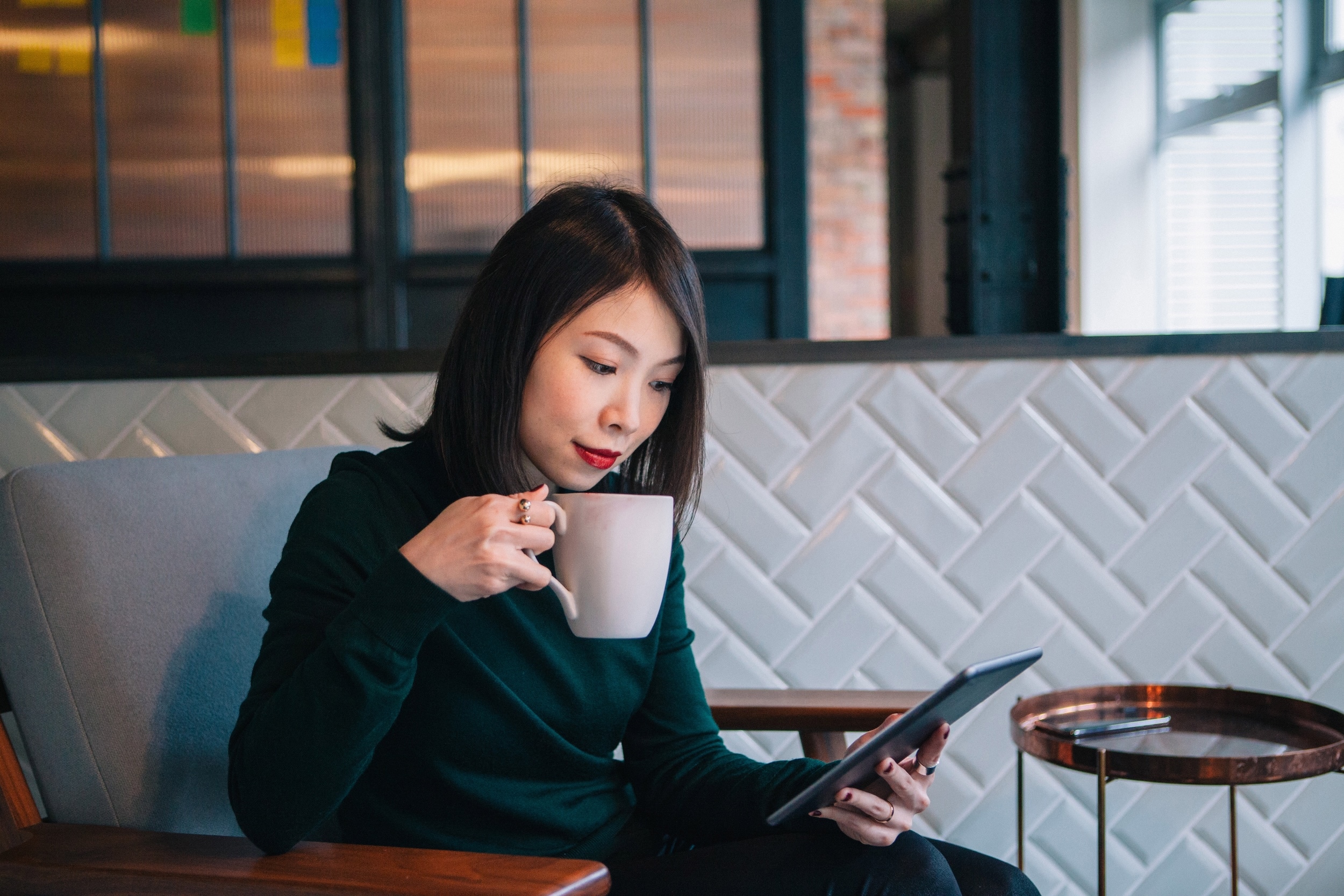 An asian woman sipping coffee and reading updates on her phone