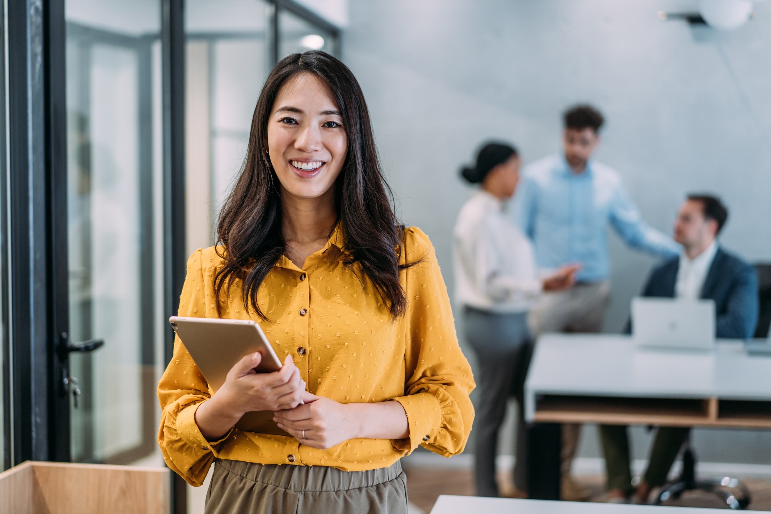 Woman in yellow shirt smiling with an ipad in a school office