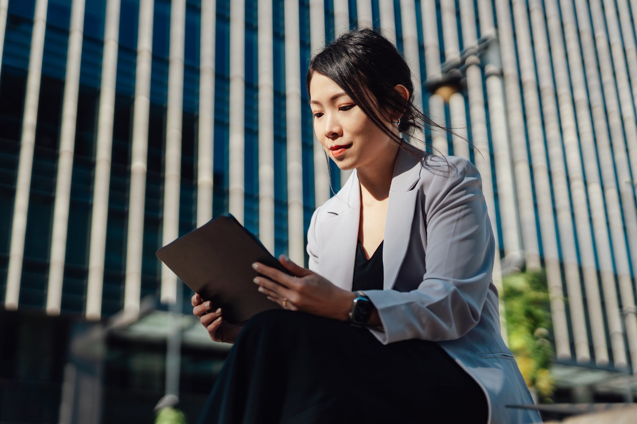 Woman sitting outside in front of a building looking at a tablet