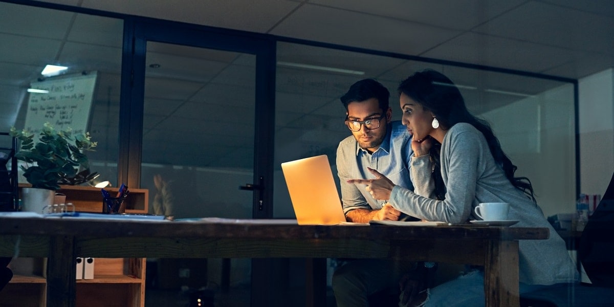 Two office workers looking over a laptop computer.