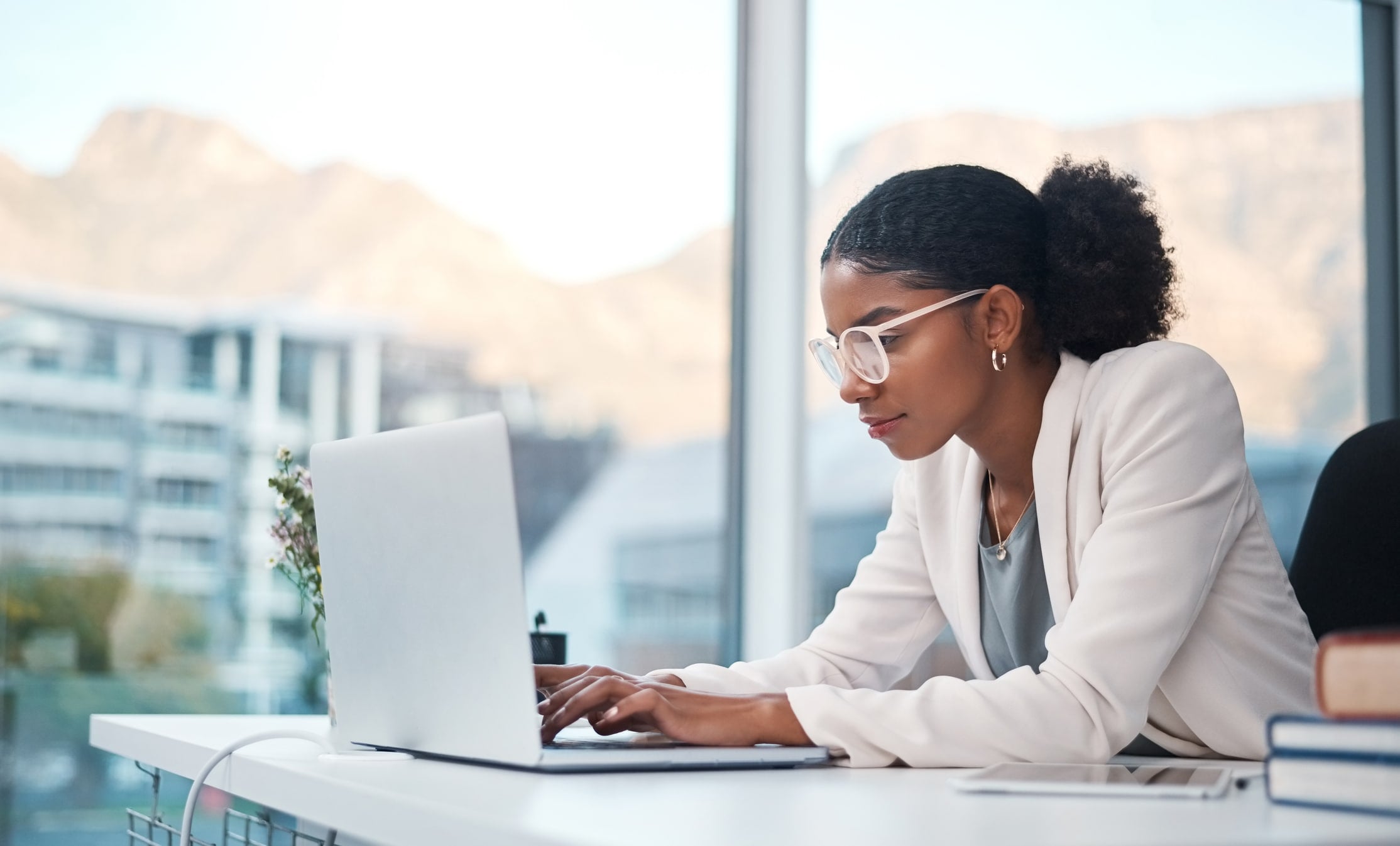 woman white coat glasses sitting at desk with laptop