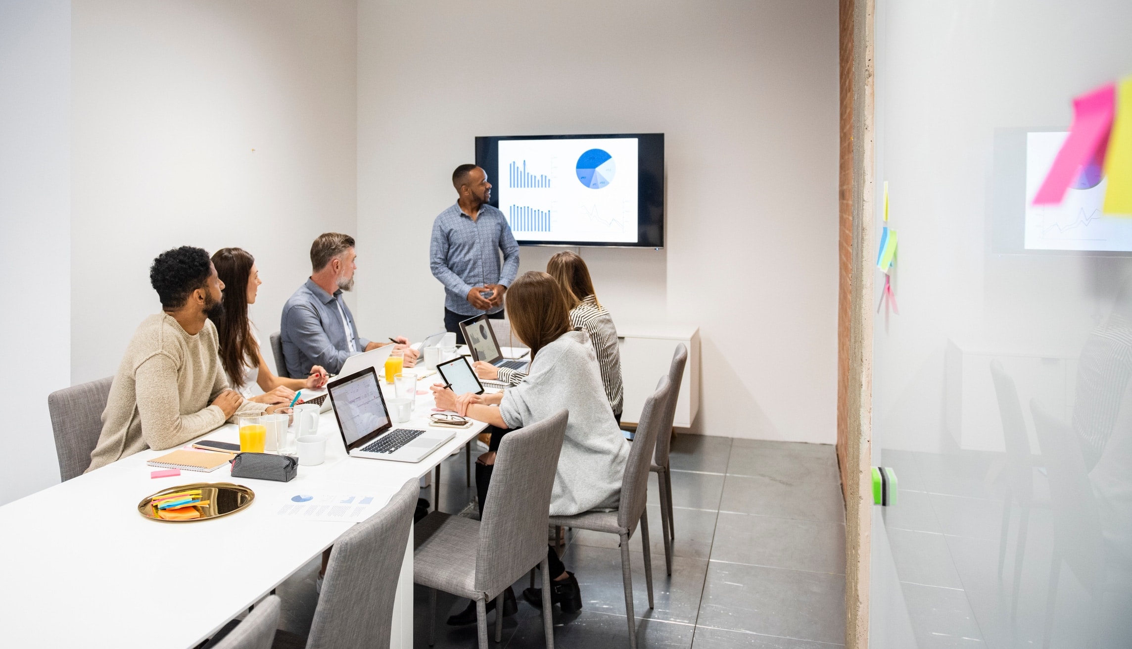 team meeting, employees sitting at a table, graph displayed on TV screen
