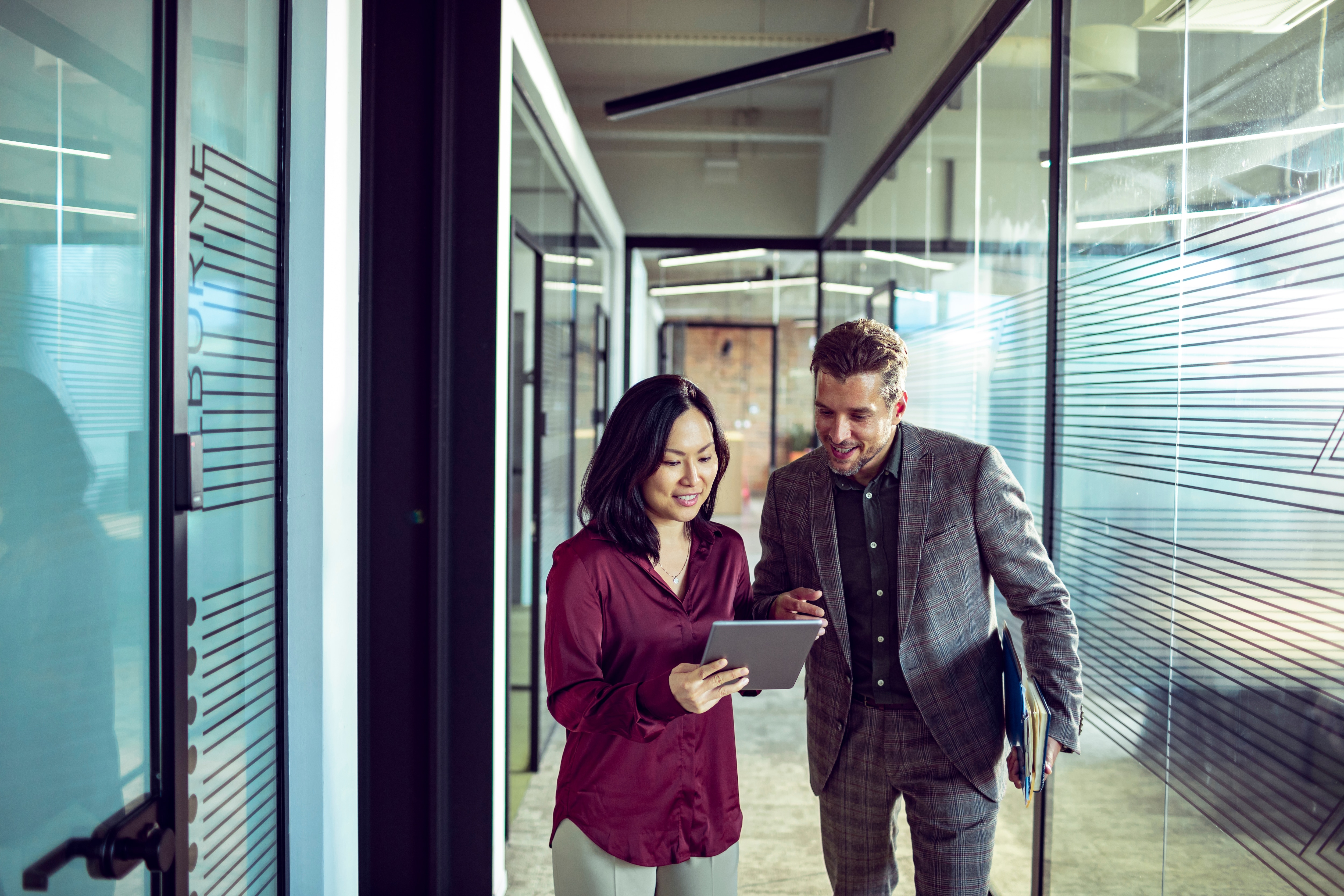 Two people walking down an office hallway looking at a tablet