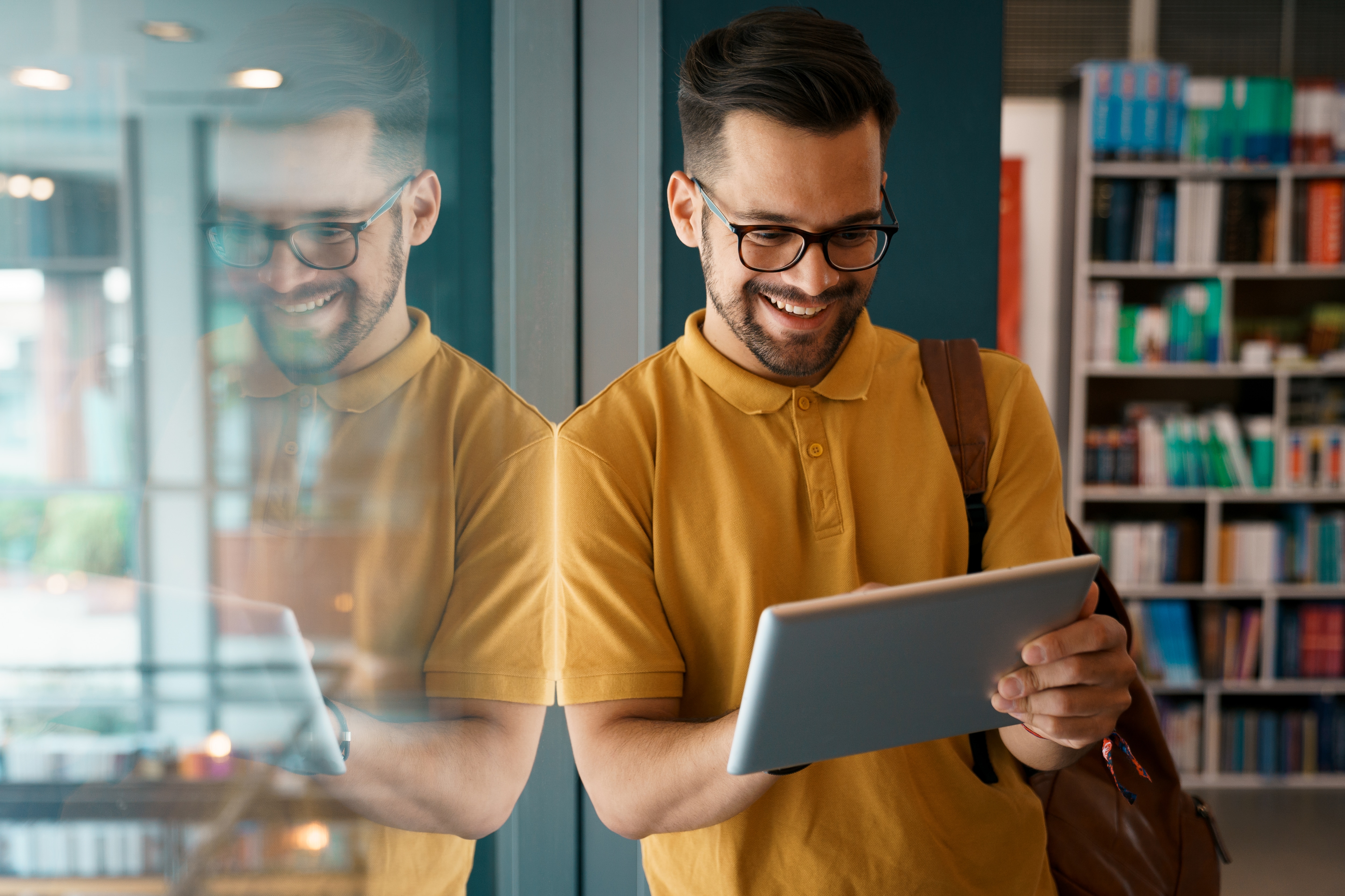 Man smiling in a library looking at a tablet