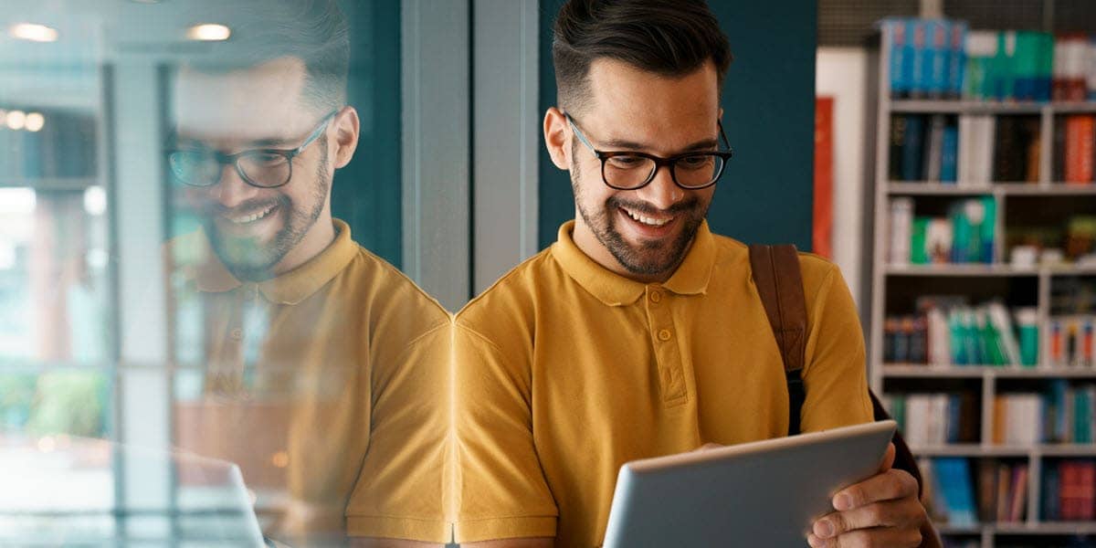 Man smiling at tablet with bookcase in background