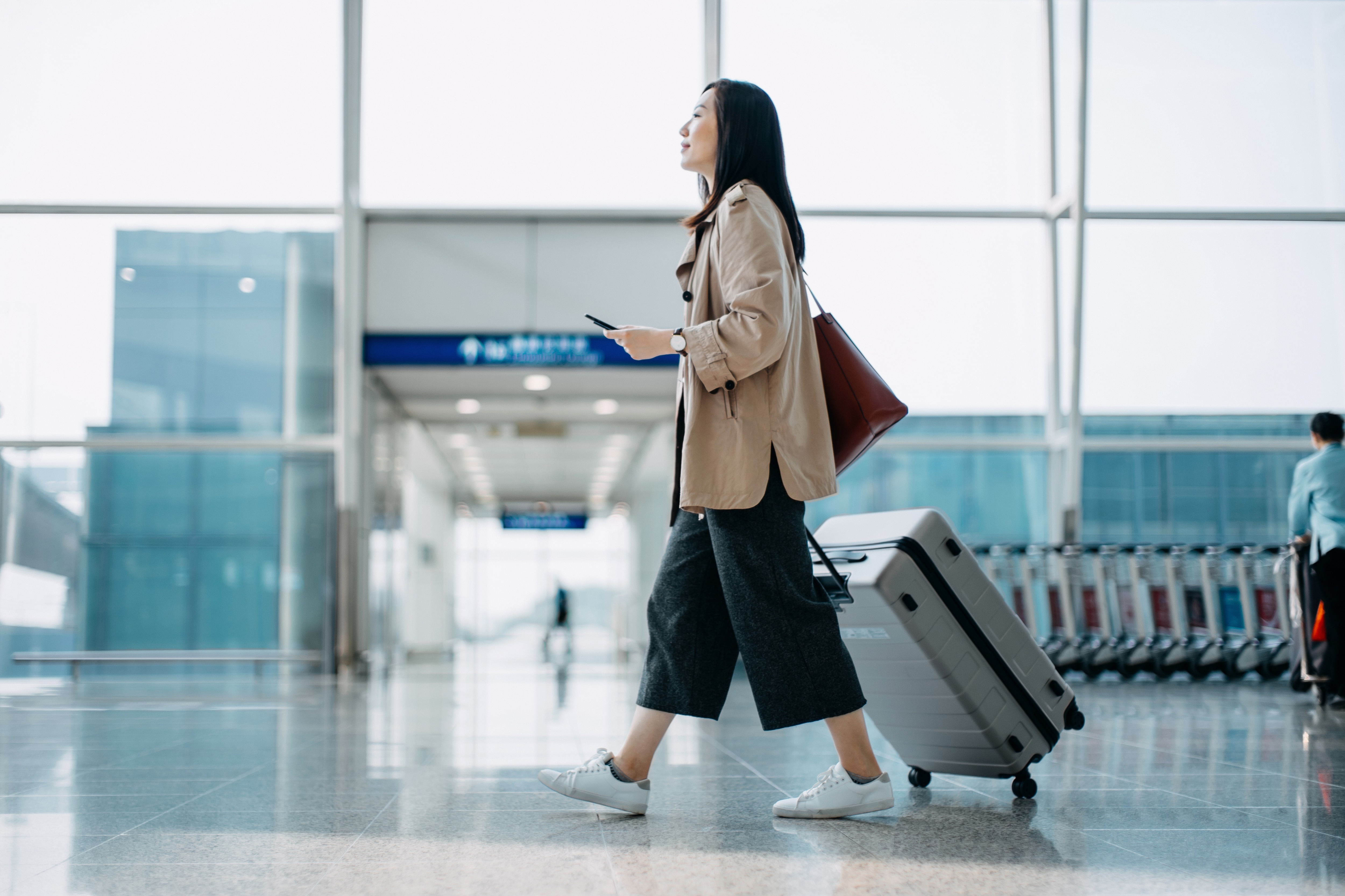 Woman walking through airport with luggage on her phone