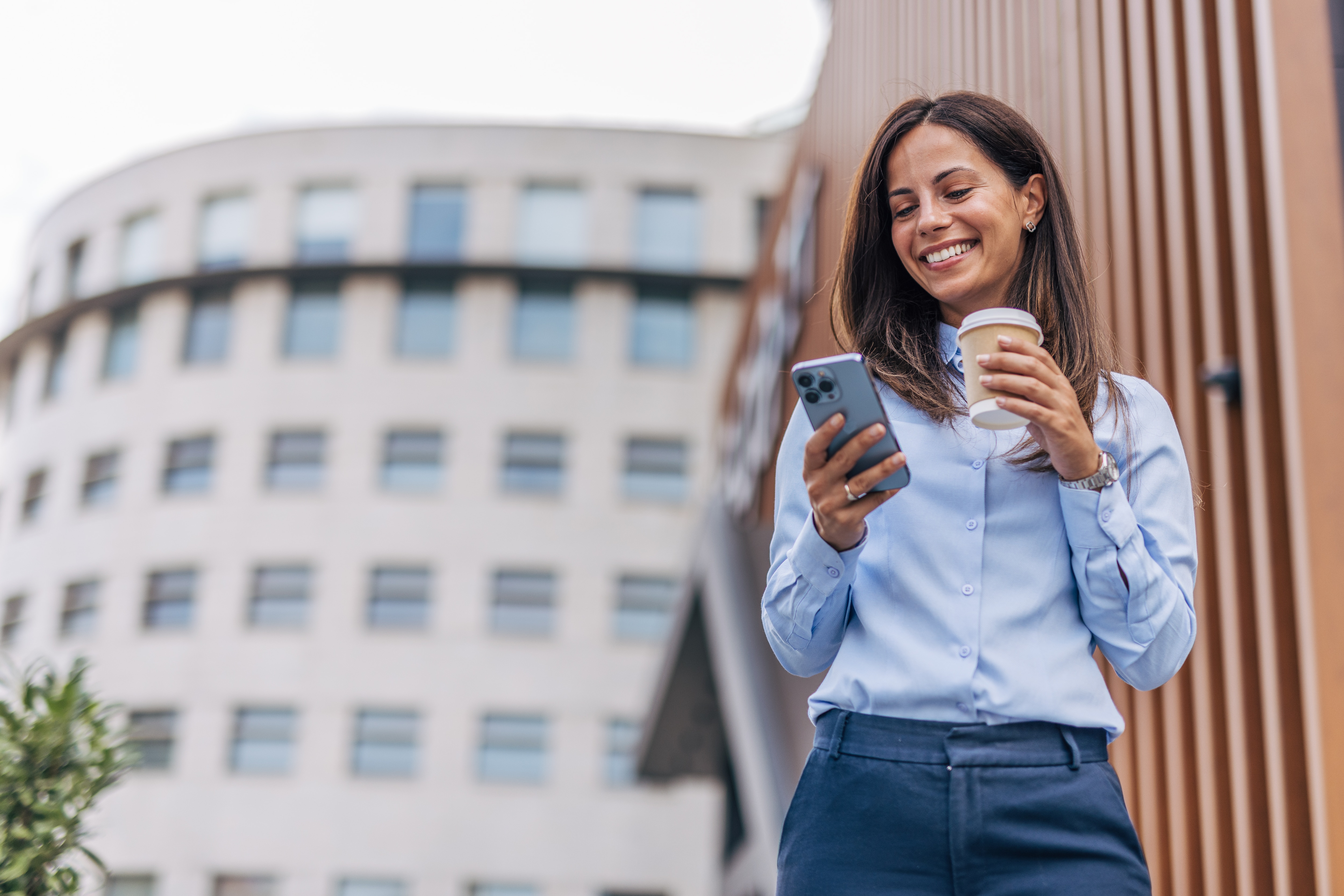 woman looking on her phone with coffee in front of a school