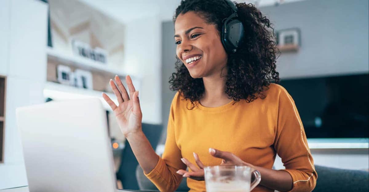 A woman waves hello while taking a video call from home
