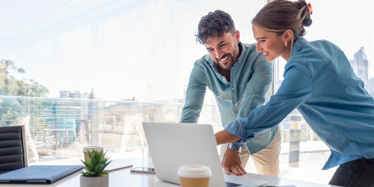 Two office workers looking over a laptop computer.