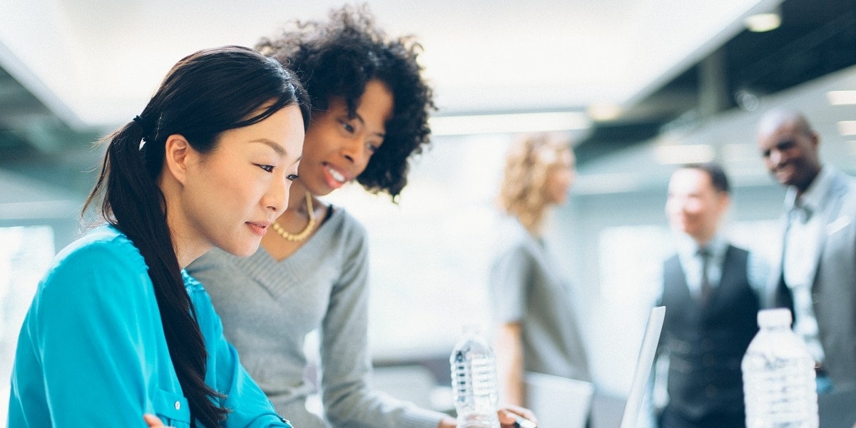 Two office workers looking over a laptop computer together.